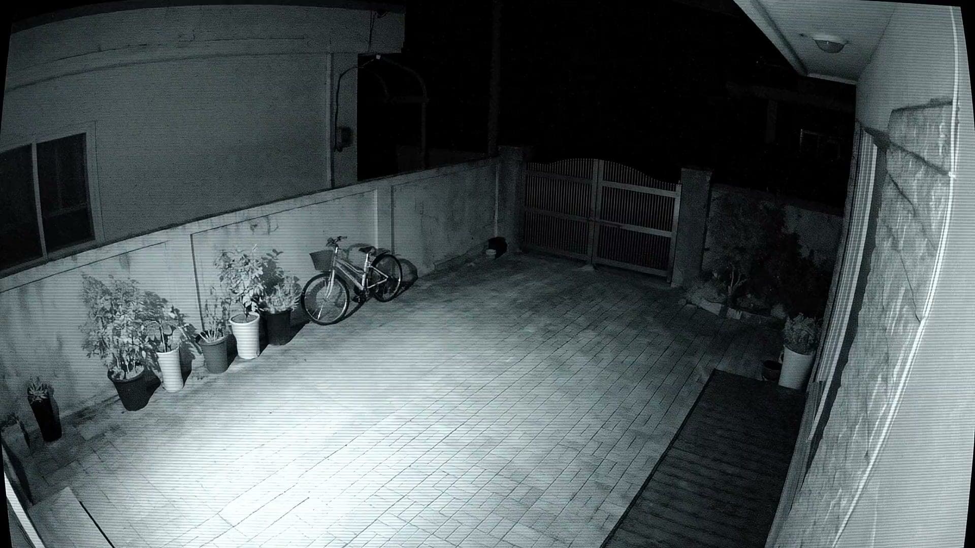 불을 끈 마당을 카메라가 흑백으로 비춘 화면. 대문과 자전거까지 보인다